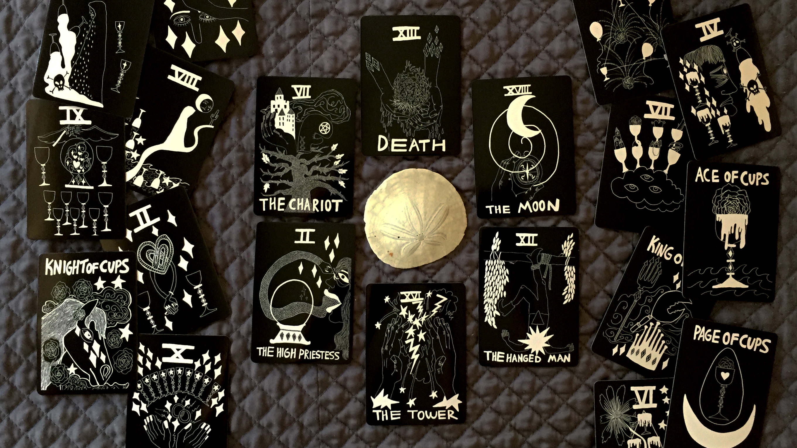 Water cards in tarot, with the Chariot, Death, Moon, Hanged Man, Tower, High Priestess, and all cards in the Cups suit arranged around a sand dollar.