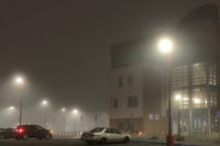 Heavy fog over streetlights in a parking lot with a building in the background