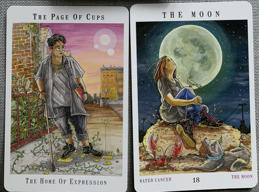 The Page of Cups and The Moon from Next World Tarot. The Page uses a cane and has paused to look at what may turn into found art on a city sidewalk; the Moon shows a woman on a rock with a bird perched on her knee, both observing the full moon as a dog and crayfish watch from the ground. 